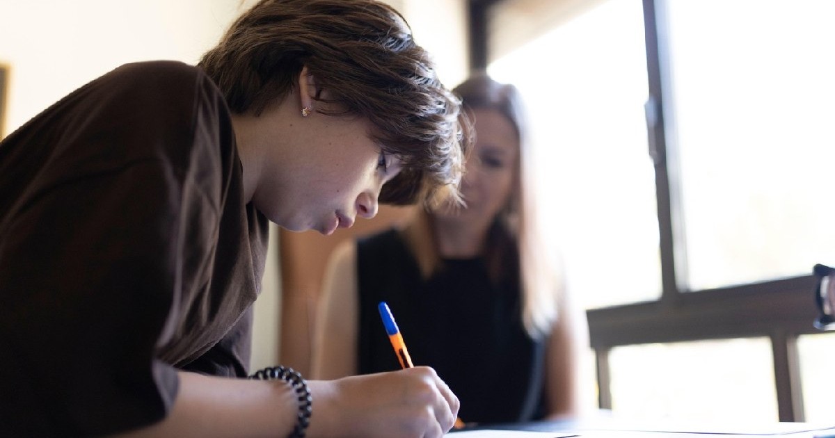 Elev care se concentrează asupra testului, scriind pe hârtie, cu ajutorul profesorului