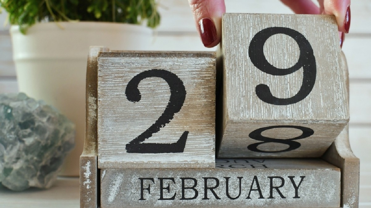 Calendar din lemn care arată data de 29 februarie, cu o mână ce mută un bloc de la 28 la 29.