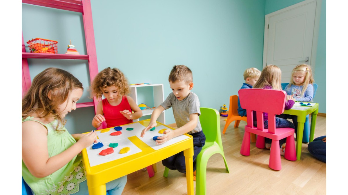 Copii de gradinita, stau la mese si coloreaza