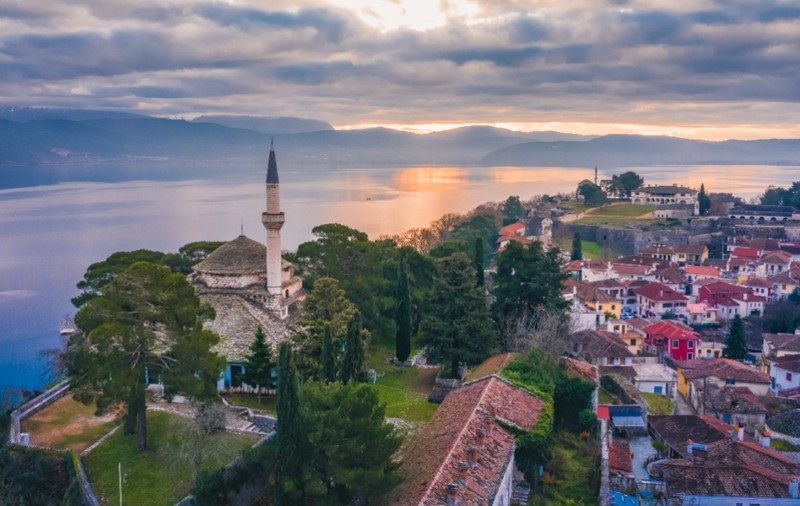 Panoramă pitorească a cetății istorice Ioannina din Grecia, situată pe o peninsulă ce înaintează în lacul Pamvotis, cu moscheea Fethiye și minaretul său evidențiate în prim-plan la apus.   