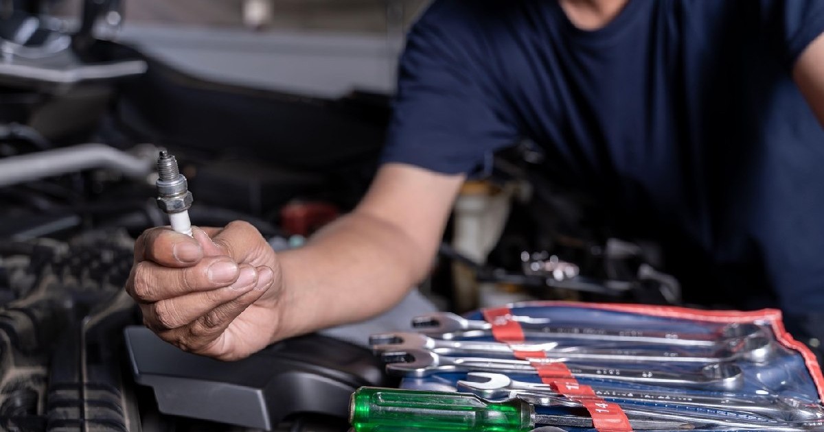 Un bărbat reparând motorul unei mașini și ținând în mână o bujie defectă