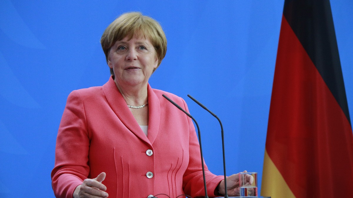 Imaginea o prezintă pe Angela Merkel, îmbrăcată într-un sacou de culoare corai sau roz intens, vorbind la un pupitru cu microfoane, având o expresie deschisă și zâmbitoare. În spatele ei se află un fundal de un albastru viu și, parțial vizibil, drapelul Germaniei pe partea dreaptă.