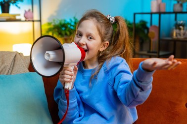 Preteen child girl talking with megaphone, proclaiming news, loudly announcing advertisement, warning using loudspeaker to shout speech. Caucasian female kid at home evening room apartment on sofa,Image: 1024970216, License: Royalty-free, Restrictions: , Model Release: yes
