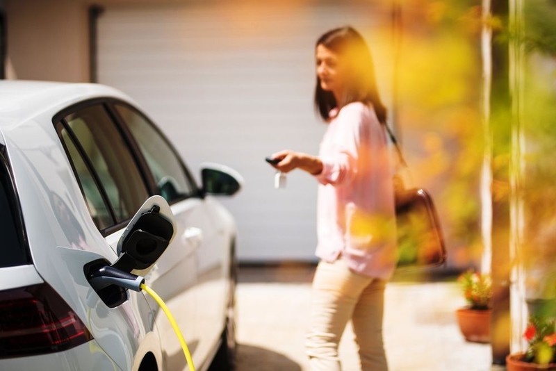 Close up of a electric car charger with female silhouette in the background, locking a car