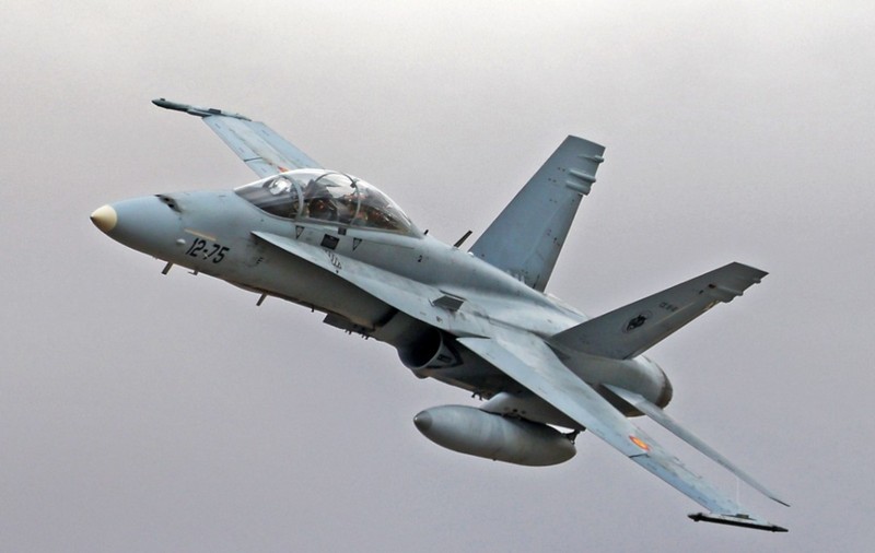 Un avion de luptă F/A-18 Hornet surprins în zbor în timp ce efectuează o manevră de urcare pe un cer înnorat.   