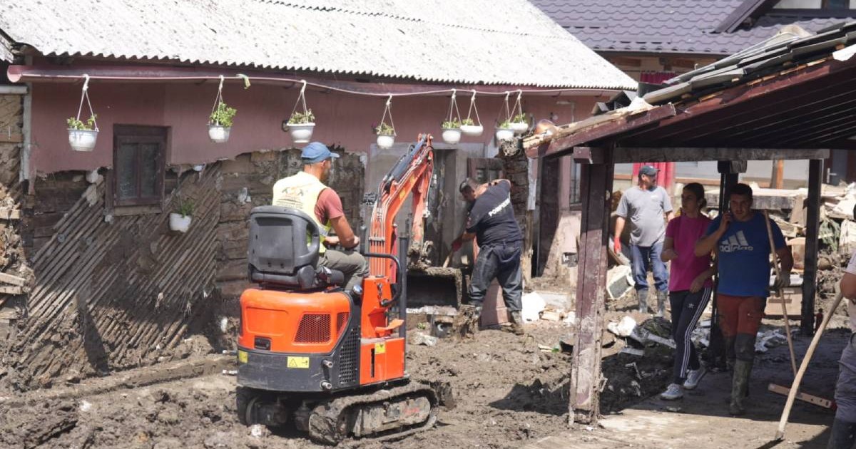 Voluntarii și pompierii lucrează cu un excavator pentru a scoate noroiul dintr-o curte din Broșteni
