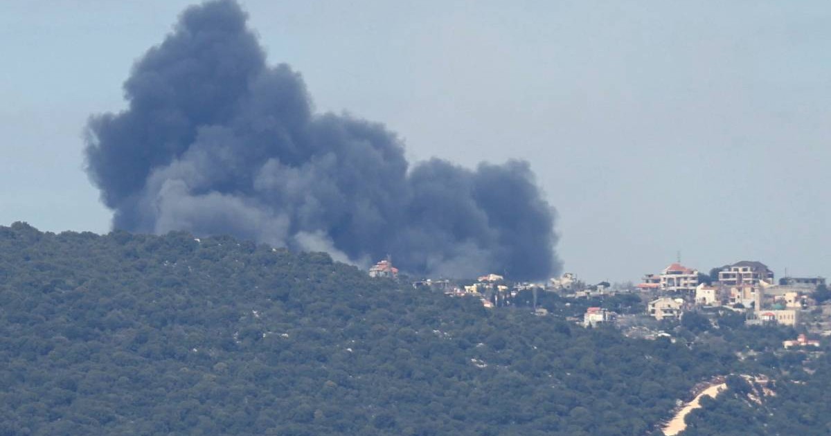 imagine cu un oras micut peste un deal de padure, se observa fum negru in urma unui atac
