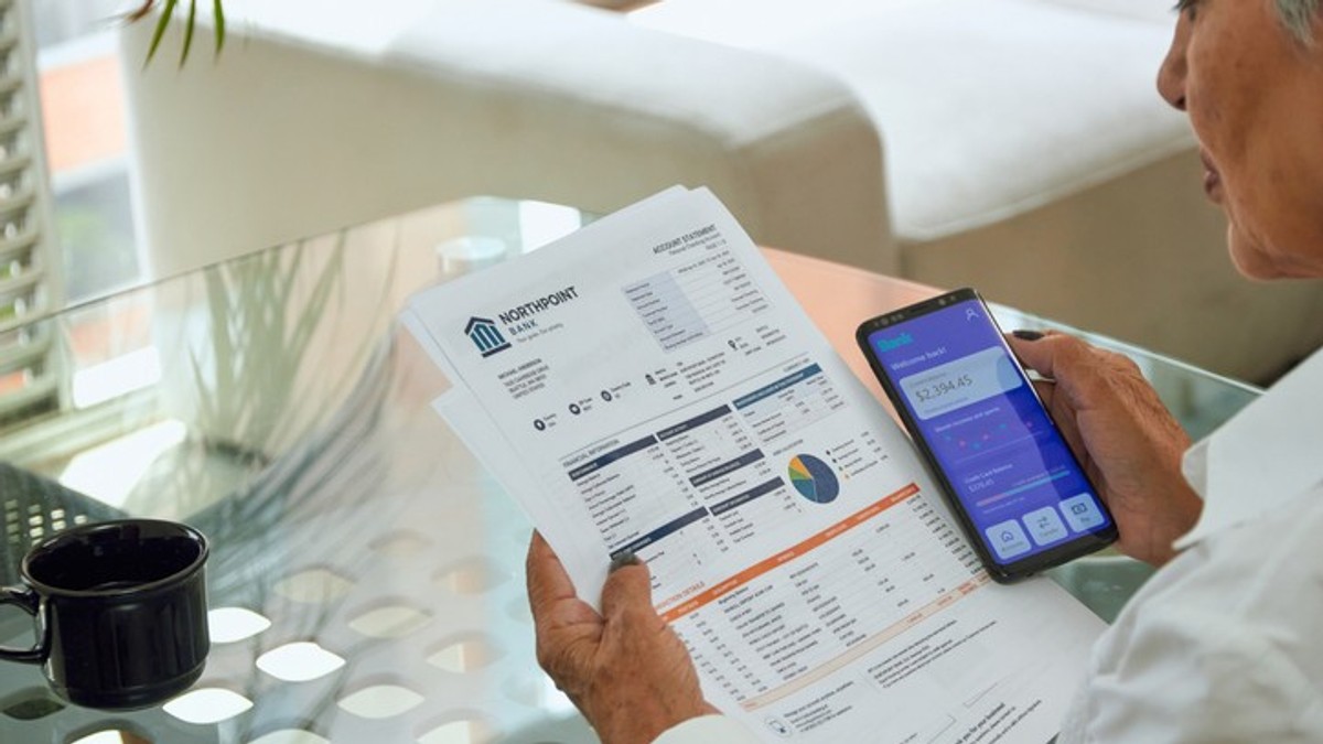 A senior woman pays her utility bills through the banking app on her phone.