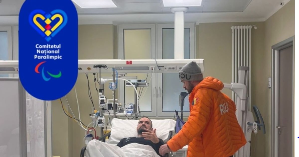 Un bărbat este întins pe un pat de spital, conectat la echipamente medicale, într-o sală de tratament. Lângă el se află o altă persoană îmbrăcată într-o geacă portocalie, care pare să discute cu pacientul, în timp ce în colțul imaginii apare logo-ul Comitetului Național Paralimpic.