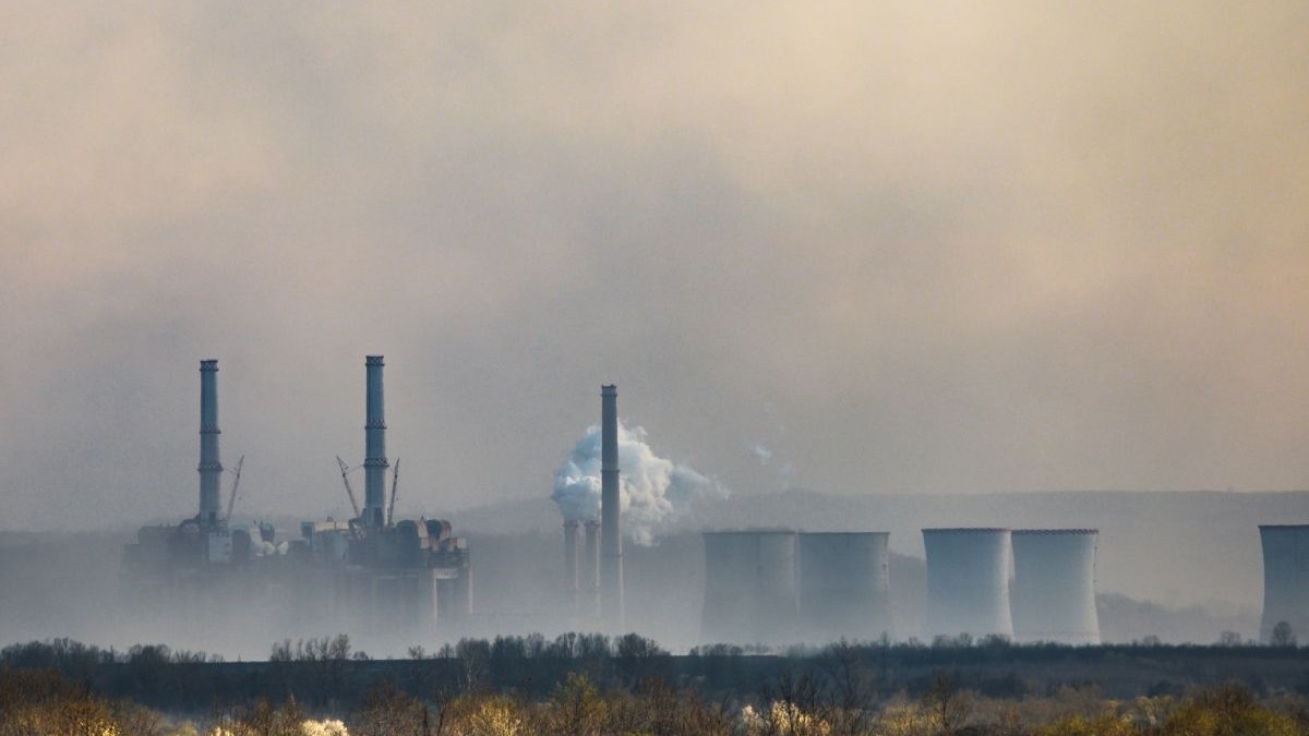 Imagine creativă cu coșurile unei termocentrale, care scot fum, iar pe fundal cerul la apus, cu nori închiși la culoare