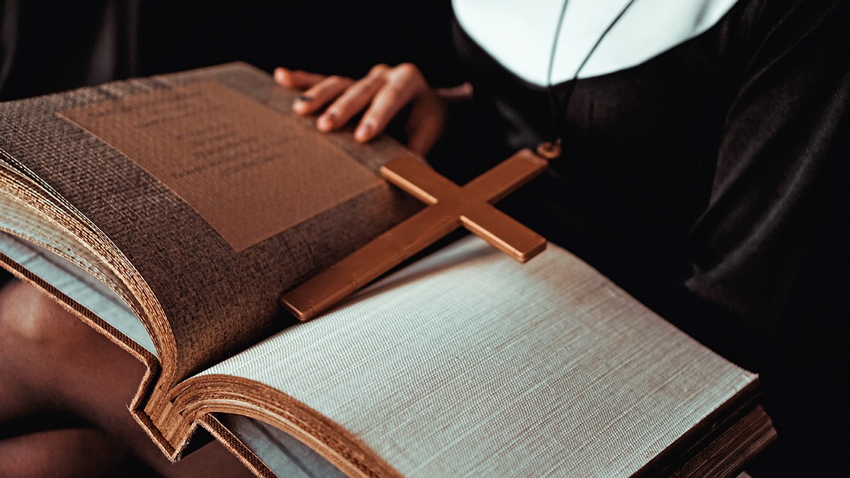 Călugăriță în costum negru religios ține Biblia și pozează în fața camerei cu o carte mare pe fundal negru. Prim-plan. Concept de religie