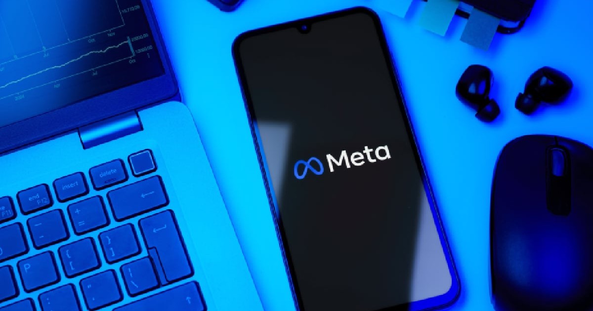 Pe o masă sunt așezate un laptop, un telefon mobil care are pe fundal logo-ul Meta, un mouse și o pereche de căști
