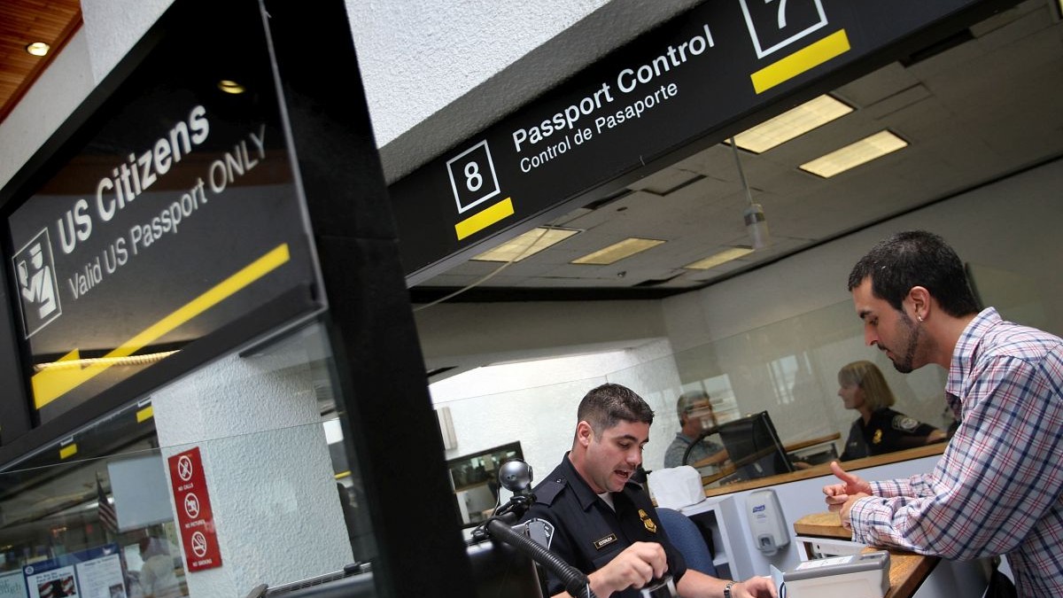 Un vameș verifică pașapoartele la cabina de control al pașapoartelor, în timp ce oamenii intră în Statele Unite prin Aeroportul Internațional Miami, pe 22 iunie 2007, în Miami, Florida