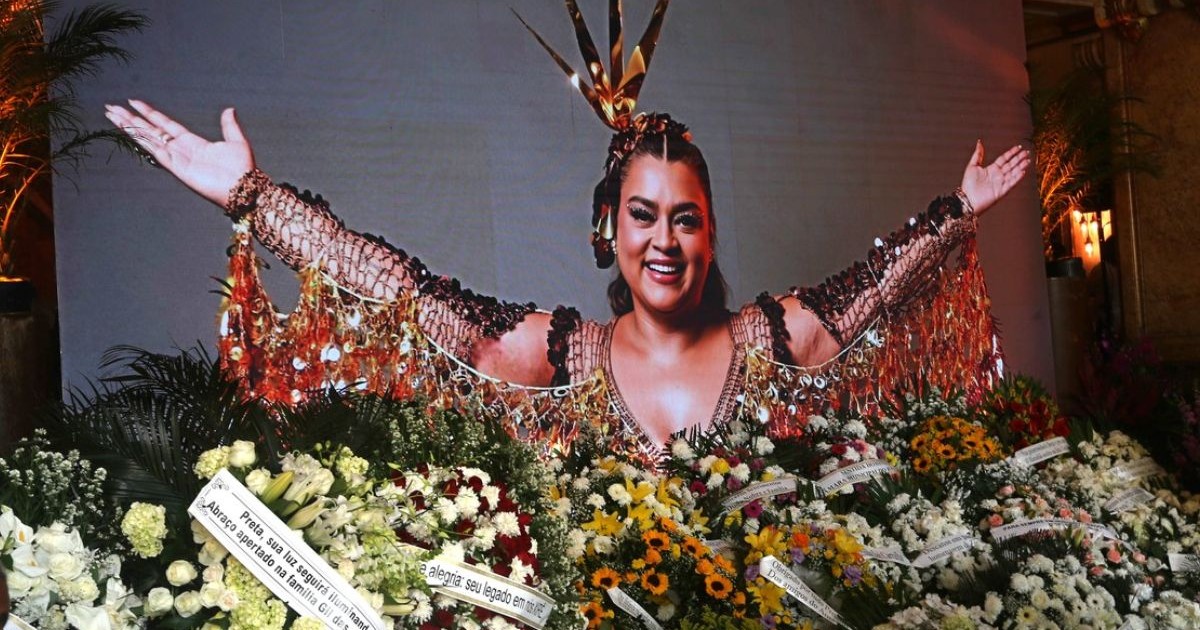 Imagine cu o fotografie a cântaretei braziliene Preta Gil, cu mainile deschise, inconjurată de flori, coroane și mesaje. Preta Gil, fiica lui Gilberto Gil, a murit pe 20 iulie 2025