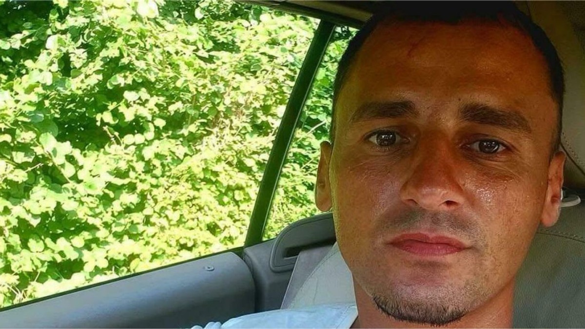 Un bărbat tânăr este fotografiat într-o mașină, iar în stânga se văd niște frunze verzi
