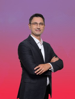 Antonio Momoc, profesor de comunicare la Universitatea din București, trainer de vorbire în public, îmbrăcat cu cămașă albă și sacou nergu, pe un fundal roz și mov.