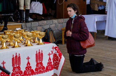 O femeie se roagă în genunghi pe scena goală de la altar. În stânga, cupele aurii în care a fost ținută pâinea pentru împărtășanie