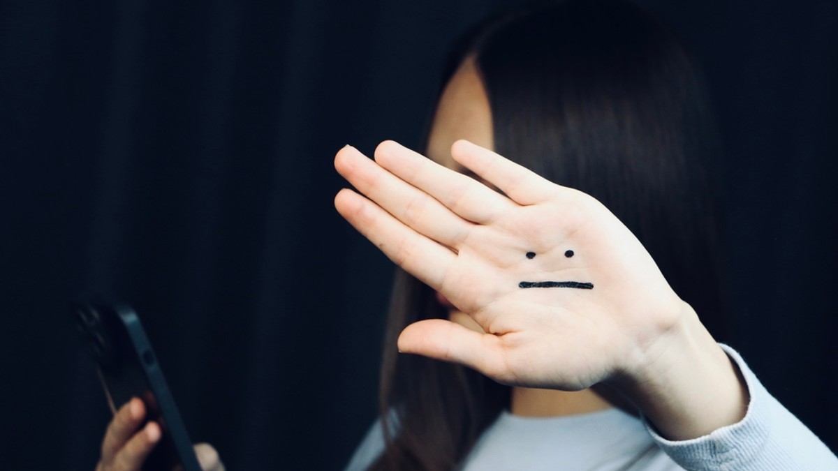 Blue Monday – cea mai deprimantă zi din an - Imagine cu o tânără care vorbeste la telefon şi îşi arată palma stângă, pe care este desenat un emoticon ce sugerează tristeţe