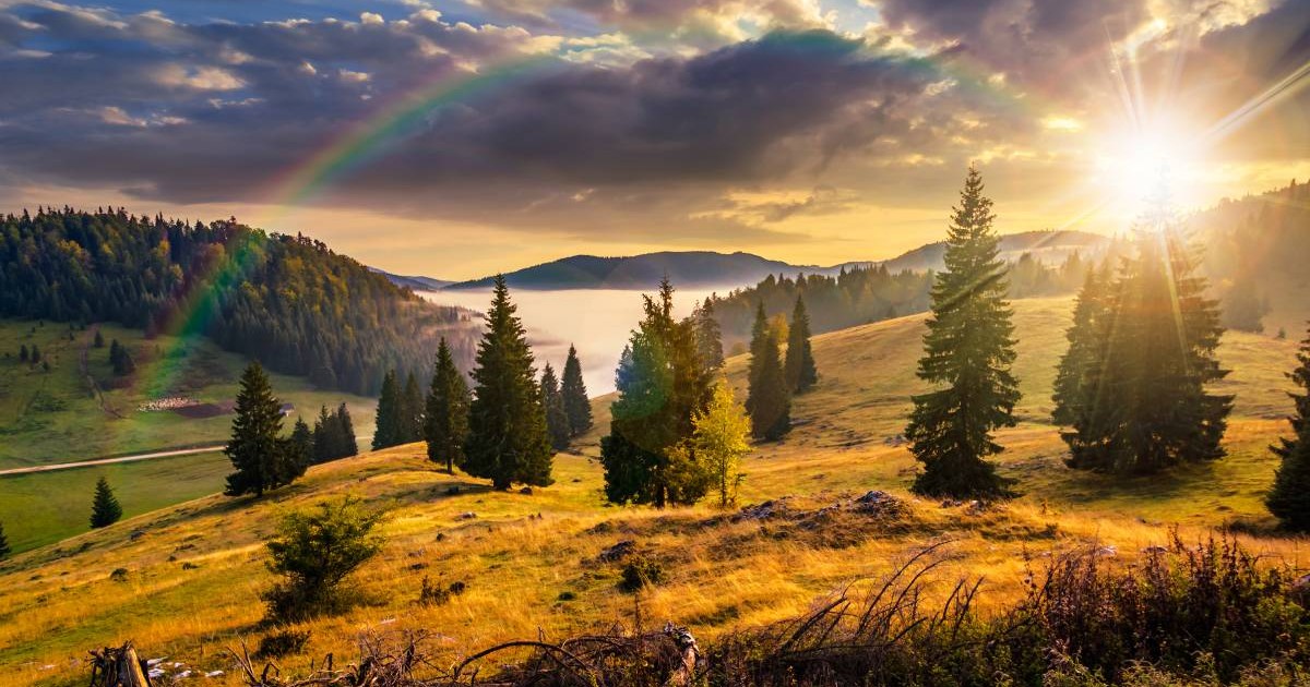 Un peisaj de toamnă la munte în România, soarele răsare peste crestele montane, iar copacii au deja frunze ruginii