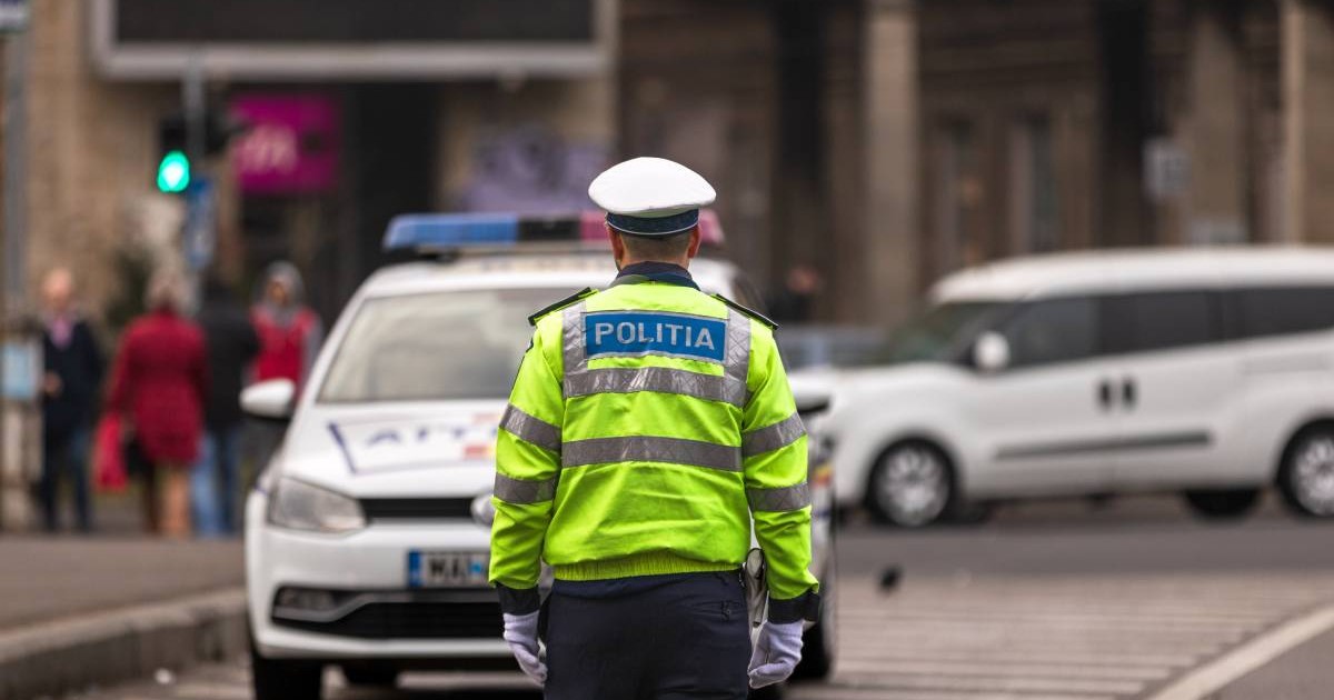 agent politie imbracat in uniforma pe fundal masina de politie