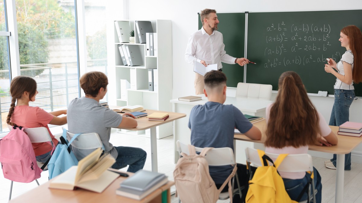 Profesor de matematica in clasa la tabla alaturi de un elev