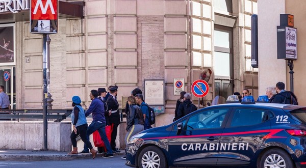 O mașină de Carabinieri oprită în dreptul unei stații de metrou din Milano, mai mulți turiști în haine groase coboară pe scările de la metrou