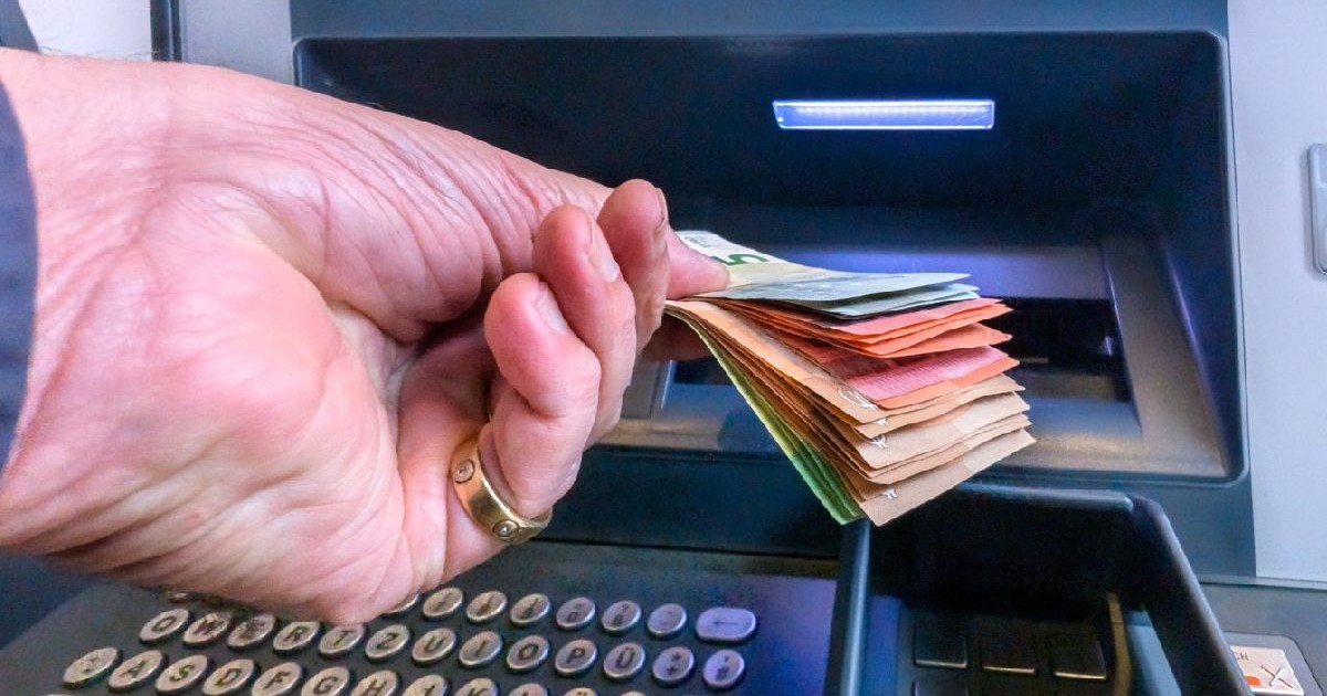 Un bărbat retrage un teanc de bancnote din bancomat