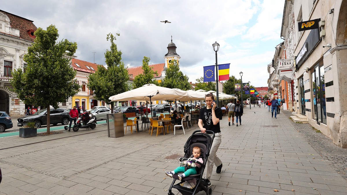 CLUJ, ROMÂNIA - 27 IULIE: O mamă și copilul ei trec pe lângă clădiri istorice în timp ce viața de zi cu zi continuă în al doilea cel mai mare oraș din România, la granița cu Ungaria, Cluj-Napoca, România, pe 27 iulie 2023.