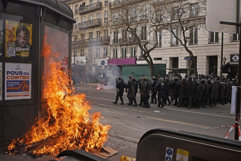 epa10538824 A kiosk is set on fire as French police officers face protesters during clashes as thousands of people participate in a protest against the government's reform of the pension system in Paris, France, 23 March 2023. Protests continue in France after the prime minister announced on 16 March 2023 the use of Article 49 paragraph 3 (49.3) of the French Constitution to have the text on the controversial pension reform law - raising retirement age from 62 to 64 - be definitively adopted without a vote. EPA-EFE/YOAN VALAT