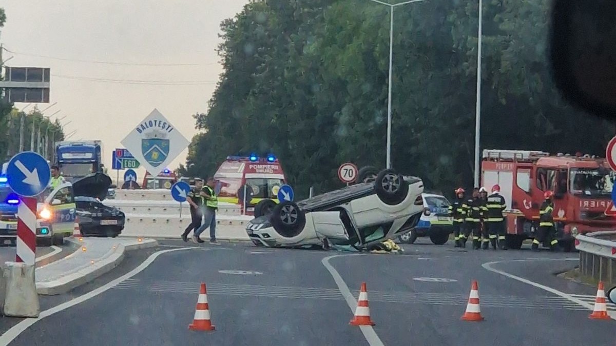 mașină SUV albă, dată peste cap în giratoriul de la intrarea în comuna Balotești, înconjurată de poliști de conuri de trafic portocalii cu dungi fosforescente. în spatele mașinii se pot observa mai multe autospeciale de salvare SMURD