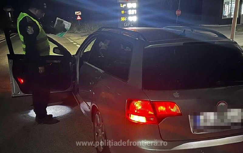 Un polițist de frontieră verifică actele unui șofer, noaptea, usa soferului este deschisă