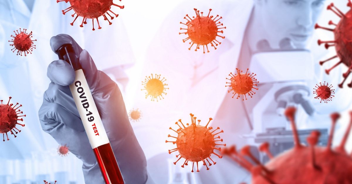 în prim-plan, o mână acoperită cu o mănușă de protecție ține un tub de testare cu lichid roșu, pe care este scris clar „COVID-19 TEST”. În jurul mâinii și a tubului apar mai multe reprezentări grafice ale unui virus de culoare roșie, cu formă sferică și proeminențe asemănătoare unor țepi. În fundal, ușor blurat, se disting persoane îmbrăcate în halate albe și un microscop, sugerând un mediu de laborator