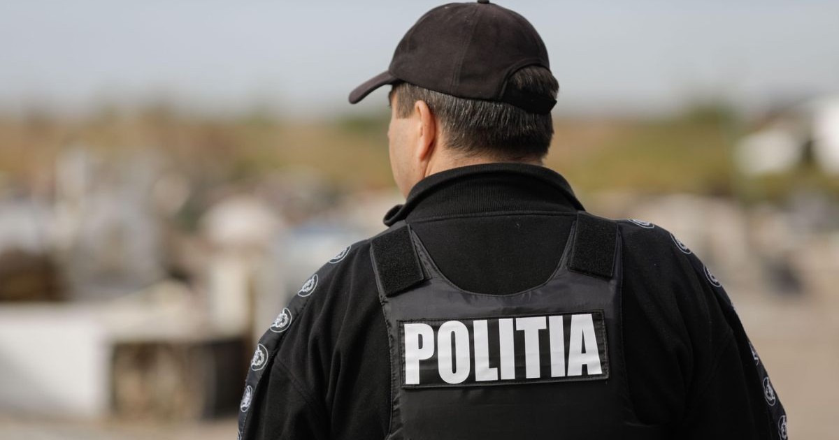 Un polițist cu vestă, îmbrăcat cu uniformă neagră, fotografiat cu spatele