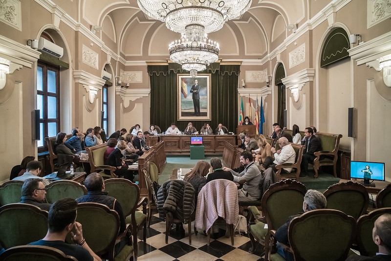 Sala de ședințe, Primăria din Castellón de la Plana. În mijloc, primarul orașului, Amparo Marco. În picioare, la pupitru (atril) vorbește românca Monica Barabas de la partidul socialist spaniol PSOE. Primul de pe rândul de sus, dreapta, este Manuel Păduraru de la partidul Ciudadanos. Ambii români sunt consilieri la Primăria din Castellón de la Plana. Tabloul din sala de ședințe îl înfățișează pe Regele Felipe al VI-lea al Spaniei.