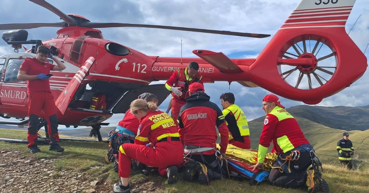 Un echipaj SMURD și salvamontiști intervin pentru salvarea unui rănit, lângă un elicopter de intervenție, pe un platou montan.