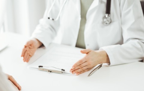 Doctorul și pacientul stând și discutând ceva unul lângă celălalt la biroul alb din clinică