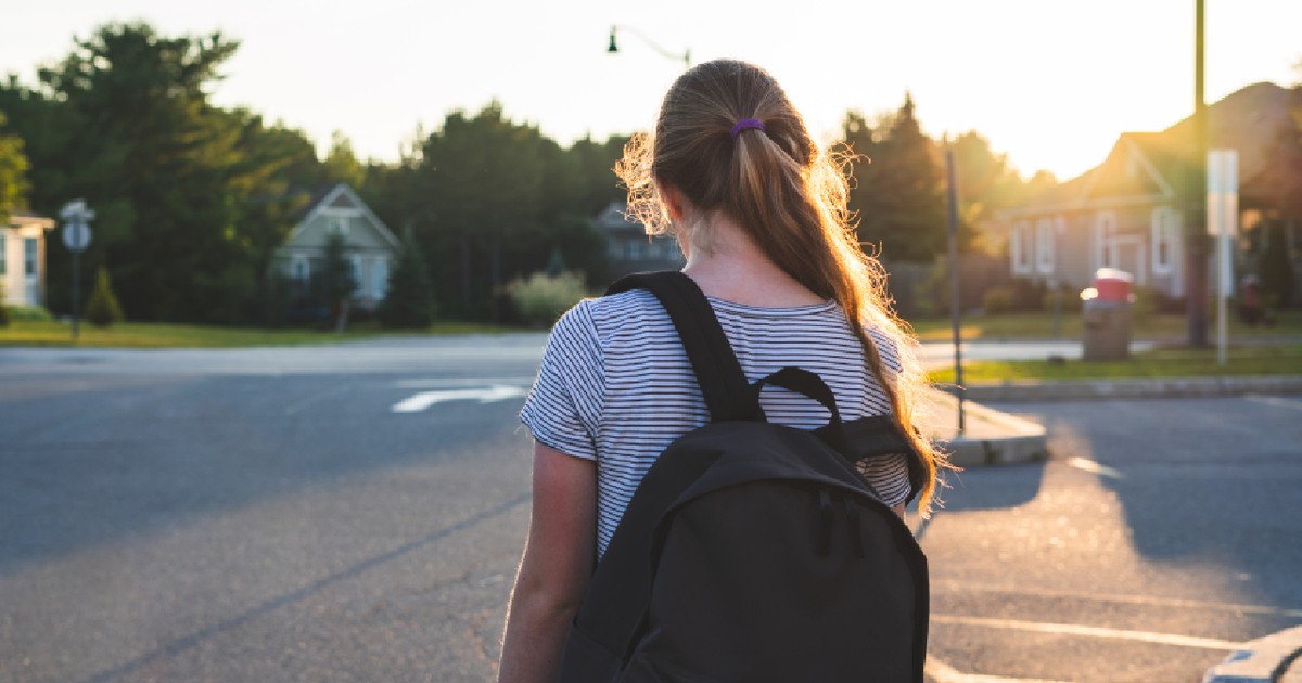 Profilul unei adolescente deprimate/triste la apusul soarelui, într-o parcare, purtând un rucsac.