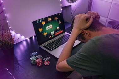 Young man play online poker in laptop. Unrecognizable person in neon light.