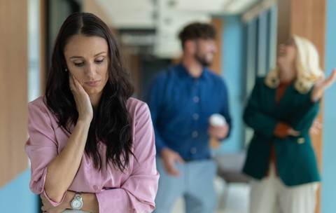 Femeie tristă care se simte singură în timp ce colegii o ignoră într-un hol modern de birou