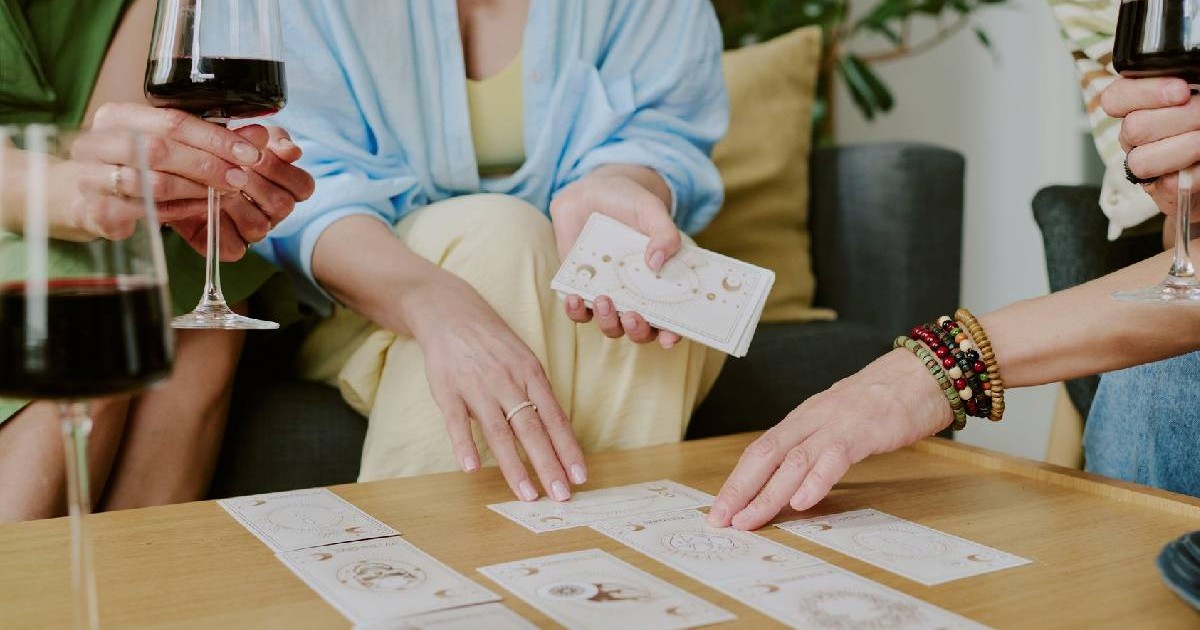 Mai mulți oameni beau vin și afișează cărțile de tarot la o masă