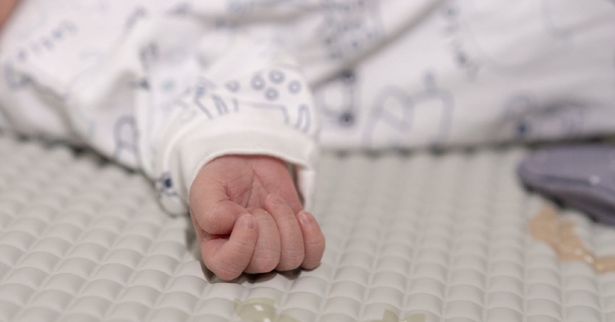 Bebeluș nou născut îmbrăcat în haine albe, întins pe o saltea