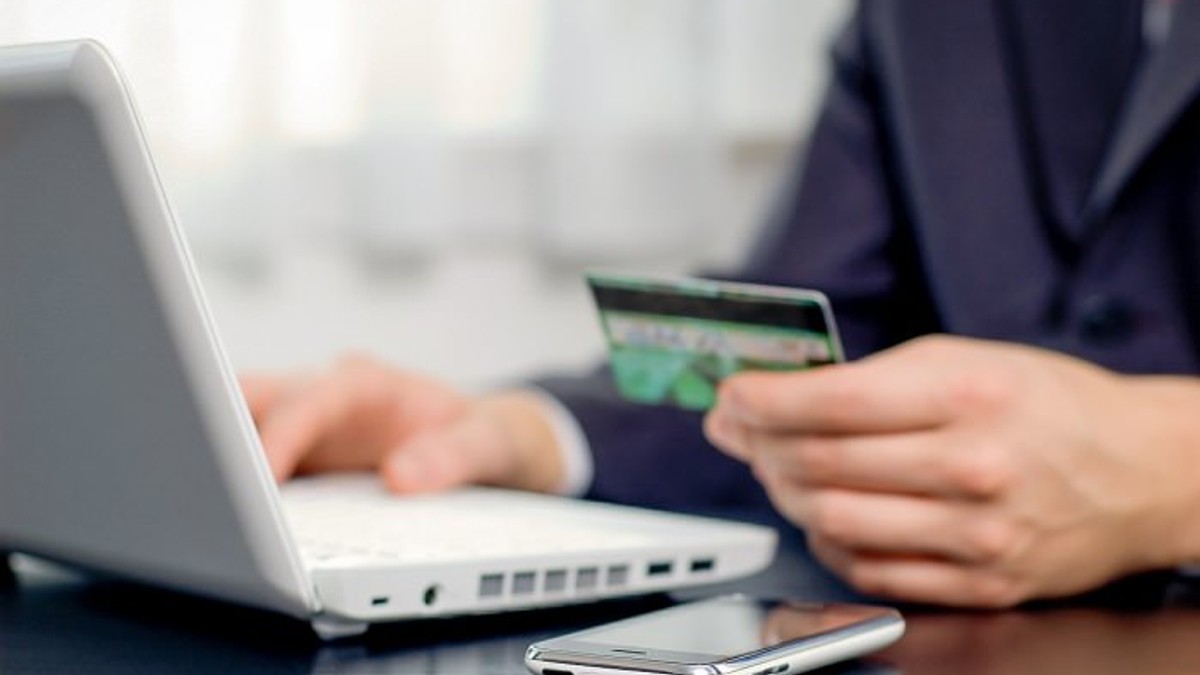 De la open source la open banking. O companie suedeză vrea să revoluționeze plățile interconectând mii de bănci. Bărbat care stă cu cardul în mână în fața laptopului