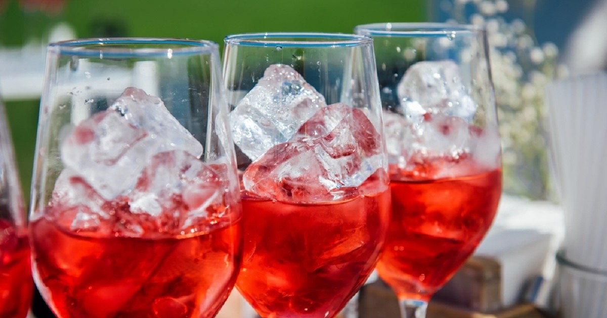 Se pune gheață în vin? Câteva pahare de vin umplute cu gheță și vin roze si puse pe un bar la o petrecere în aer liber