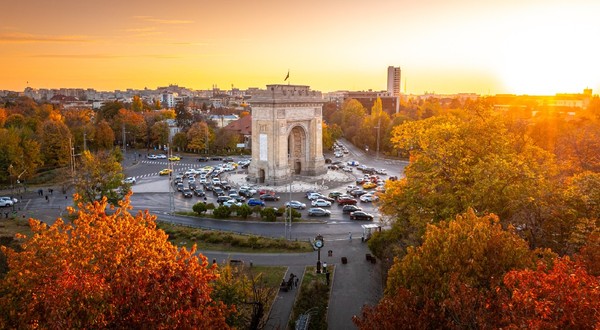 Fotografie aeriană care înfățișează Arcul de Triumf, un monument istoric din București, în timpul unui frumos apus de toamnă. 