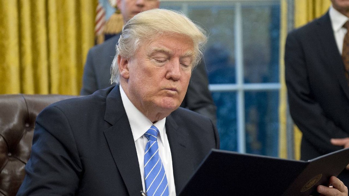 În imagine, Donald Trump citește ceva așezat la biroul de la Casa Albă