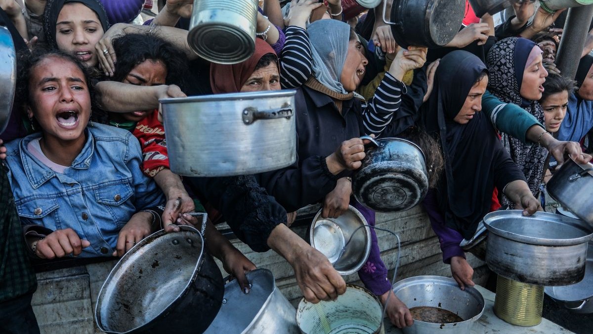 Oameni înfometați, cu oale și farfurii în mâini, în timp ce așteaptă să primească mâncare în Gaza, în ianuarie 2025
