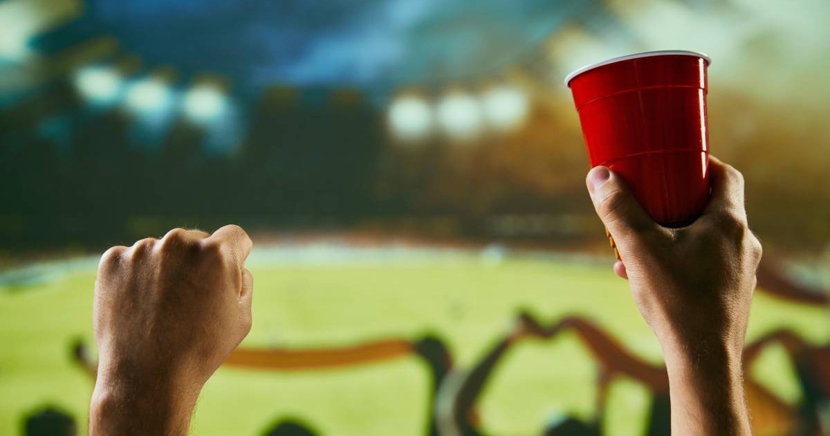 Oameni adunați pe stadion la un meci de forbal, band bere, fulare ridicate