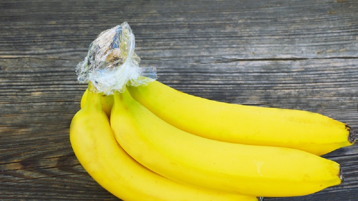 Banane galbene cu cotoarele înfășurate în folie din plastic, pe o masă din lemn.