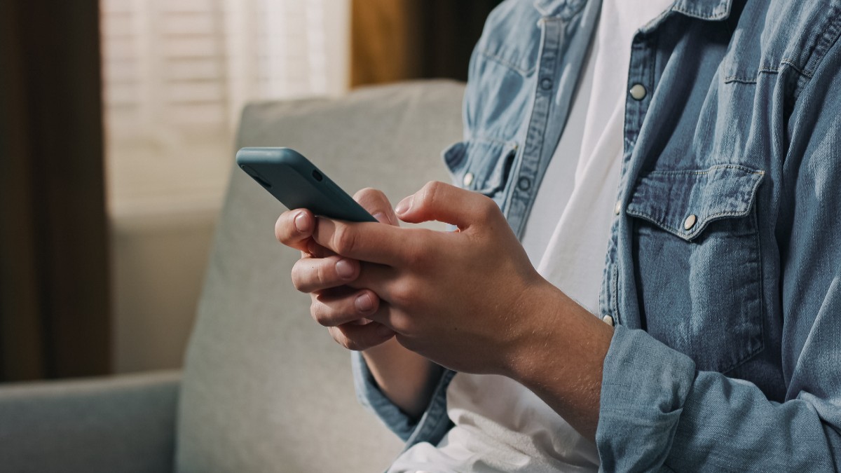 O persoană stă așezată pe o canapea și folosește un telefon mobil, concentrată asupra ecranului. Imaginea sugerează o activitate obișnuită din viața de zi cu zi, legată de utilizarea rețelelor de socializare sau a mesajelor online.