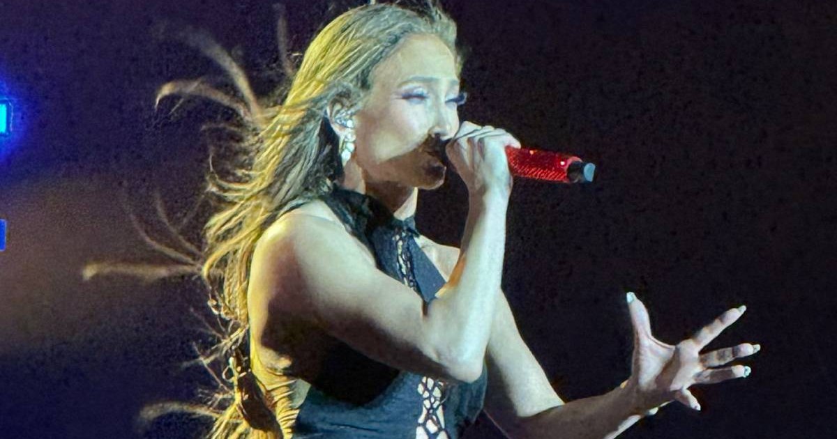 Jennifer Lopez pe scenă la București, poartă o salopetă neagră, cântă la microfon și o mână o ține îndreptate spre public